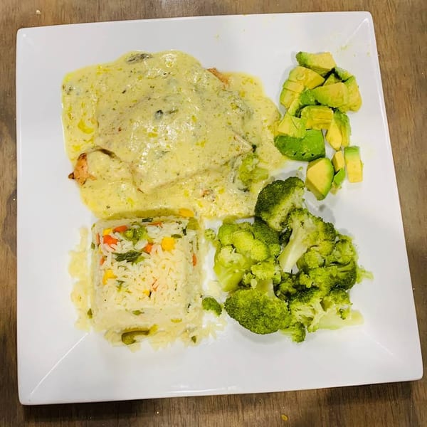 Sabor Maya's chicken in creamy sauce with rice, broccoli, and avocado on a white plate.