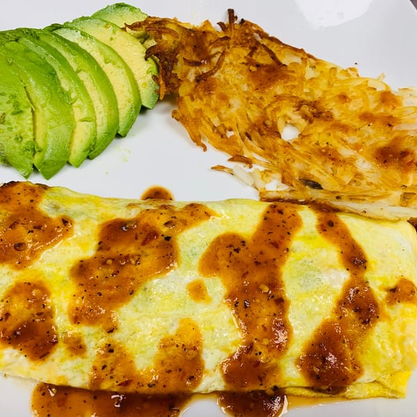 A Sabor Maya Mexican Cuisine omelet with salsa, hash browns, and sliced avocado on a white plate.
